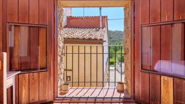 Una puerta de madera que da a un balcón con tejado de baldosas y vistas a una colina.