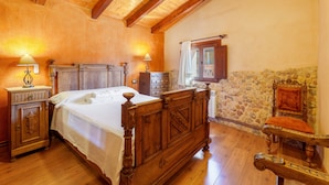 Un dormitorio con una cama de madera, una mesita de noche, un aparador, una pared de piedra y una silla.