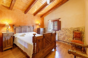 A bedroom with a wooden bed, a nightstand, a dresser, a stone wall, and a chair.