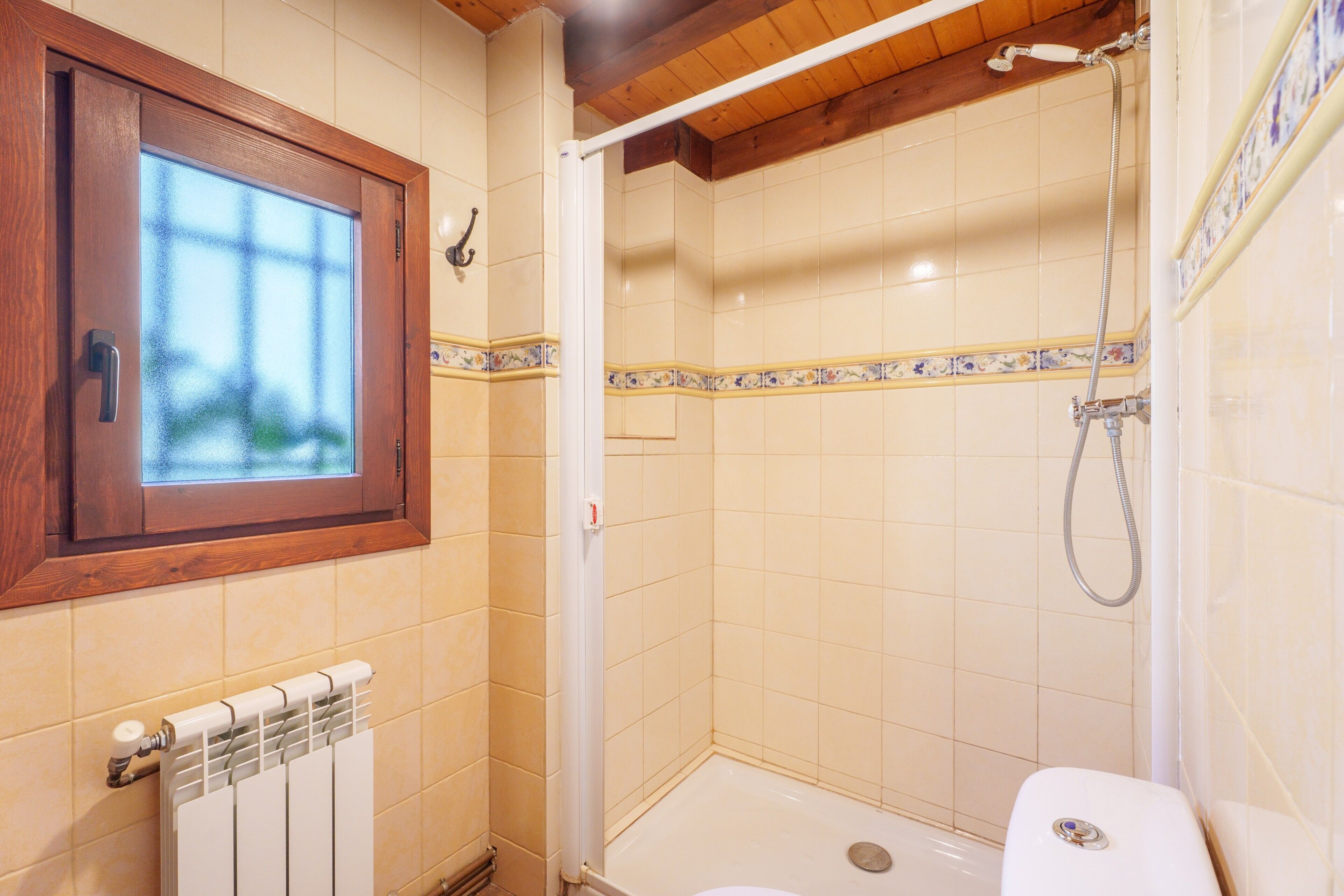 A bathroom with a shower, a toilet, a window, and a radiator.