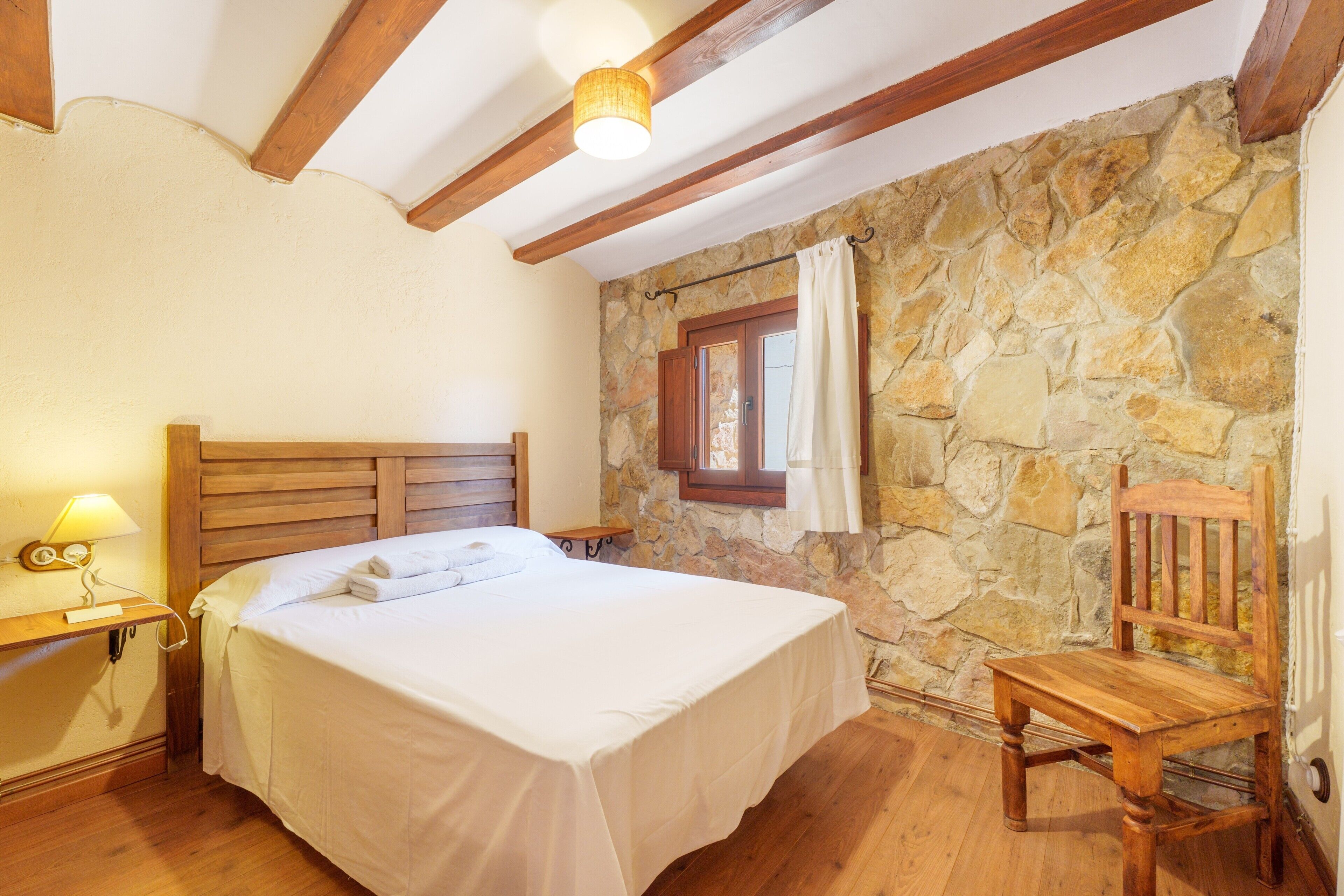 Ein Schlafzimmer mit Steinwand, Holzbettgestell und Holzstuhl.