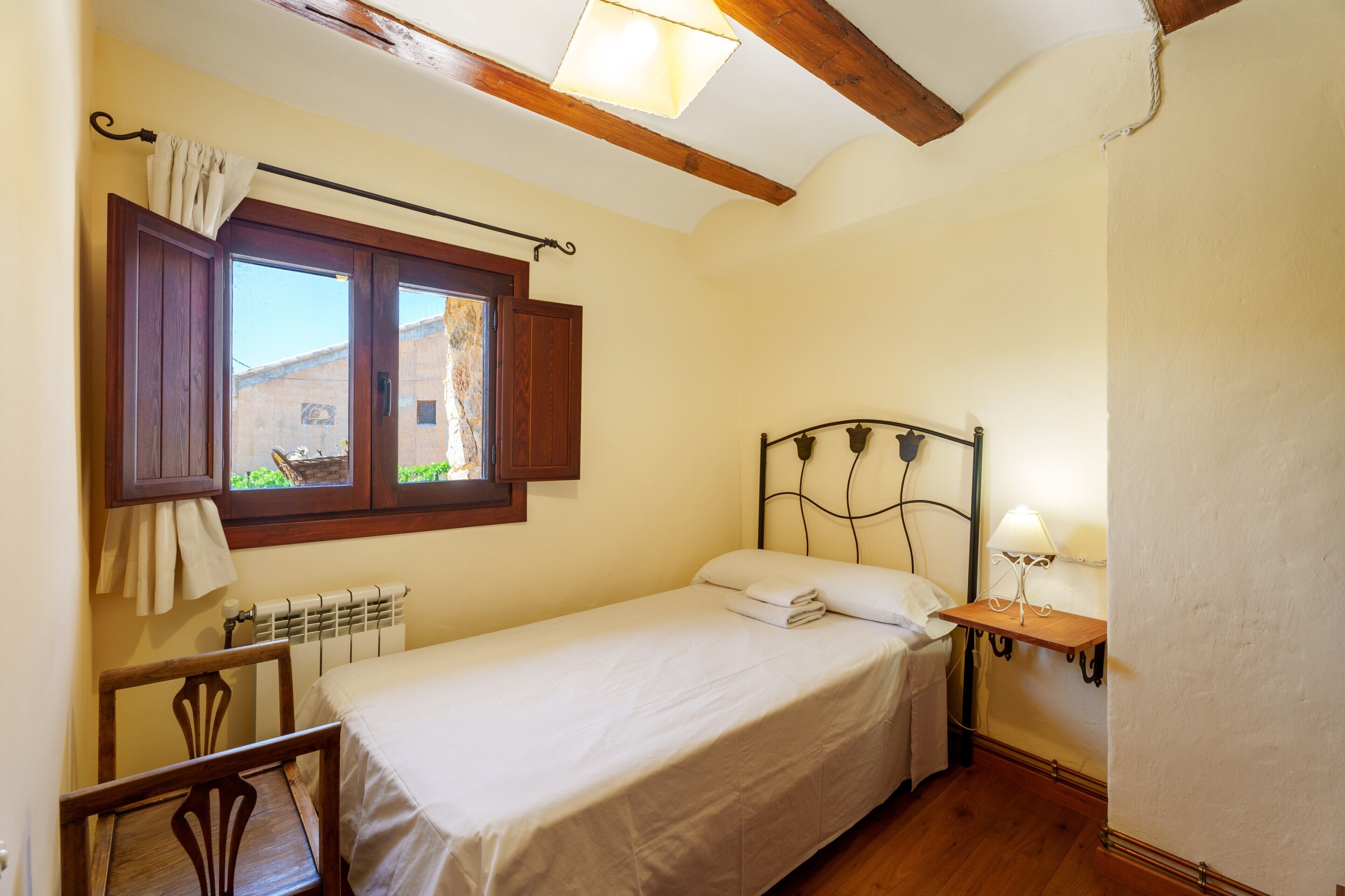 Un lit simple avec une tête de lit, une table de chevet avec une lampe, une fenêtre avec des rideaux et un radiateur.