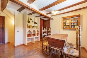 Une pièce avec une table en bois, des chaises, une étagère où sont exposées des objets en céramique et une fenêtre donnant sur un paysage.