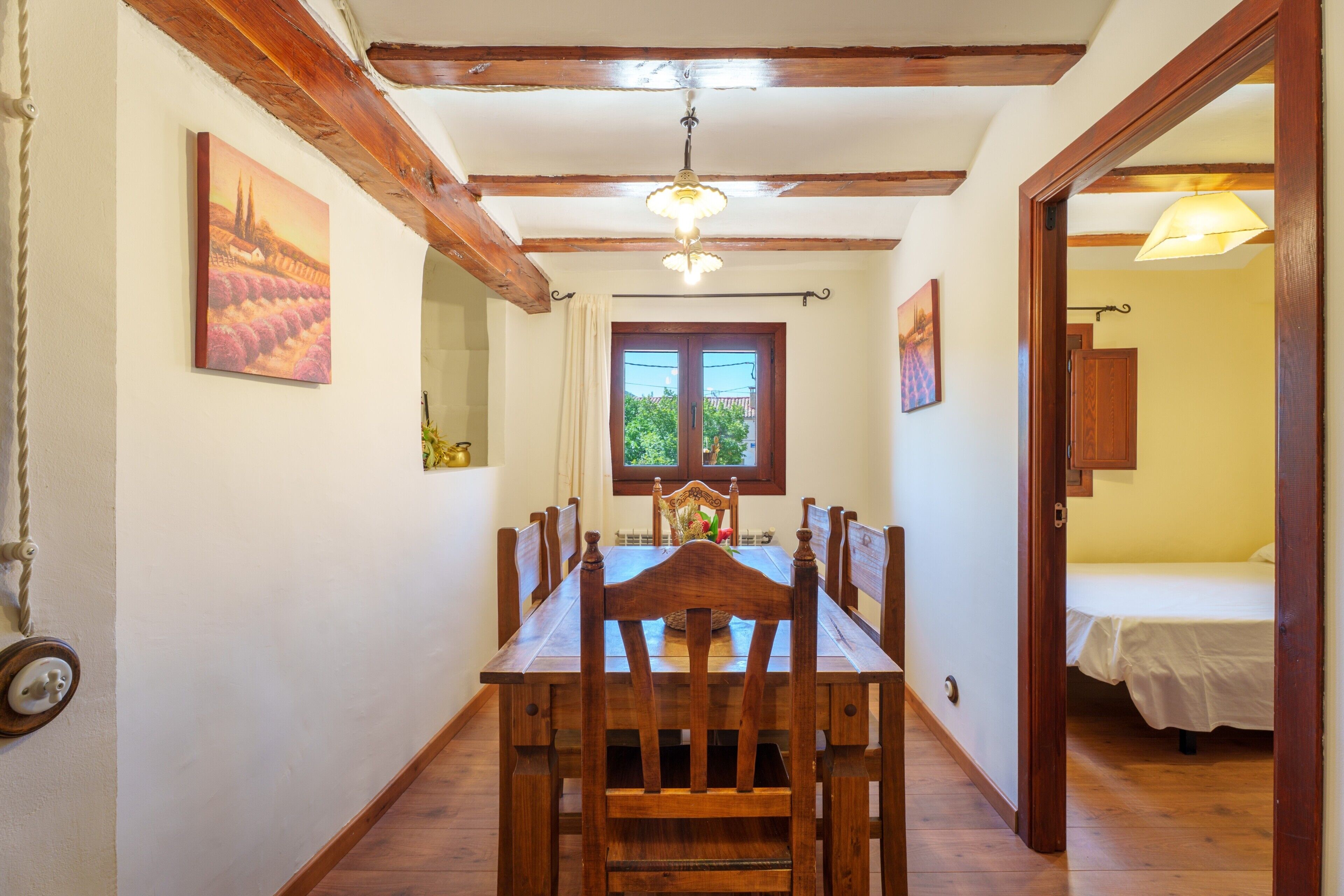 Un comedor con una mesa y sillas de madera, una araña y una ventana con cortinas.