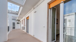 Un couloir doté de portes coulissantes en verre donnant sur des balcons, un sol carrelé et un mur blanc avec une petite fenêtre.