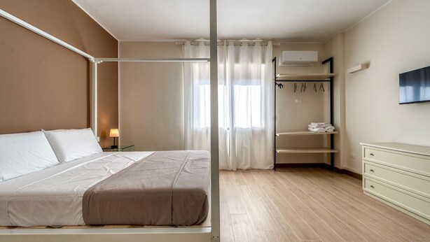 Une chambre à coucher avec un lit, une armoire, une télévision et une fenêtre avec des rideaux.
