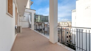 Un balcon donnant sur les immeubles voisins, un mur blanc et une rambarde en métal.