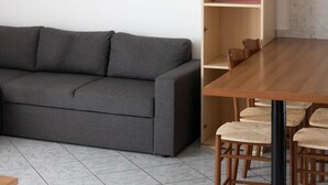 A modern living room with a grey sofa, a wooden dining table with chairs, a pink cabinet, and a beach-themed painting on the wall. - Holiday apartment mit Balkon (Jesolo)