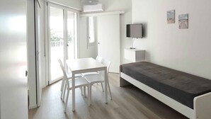 A modern, minimalist room with a white table and chairs, a grey sofa, and a ceiling-mounted light fixture. - Holiday apartment mit Balkon (Lido di Jesolo)