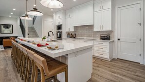 A modern kitchen with white cabinetry, a large island with bar stools, and pendant lighting. - Pecan Valley Resort|Private Pool w/Slide, Smart TV's, & Pickleball Court (Hurricane)