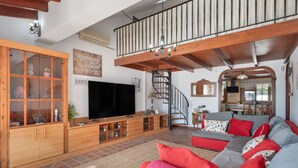 Amplia sala de estar con televisor grande, armarios de madera, una escalera y un sofá acogedor.