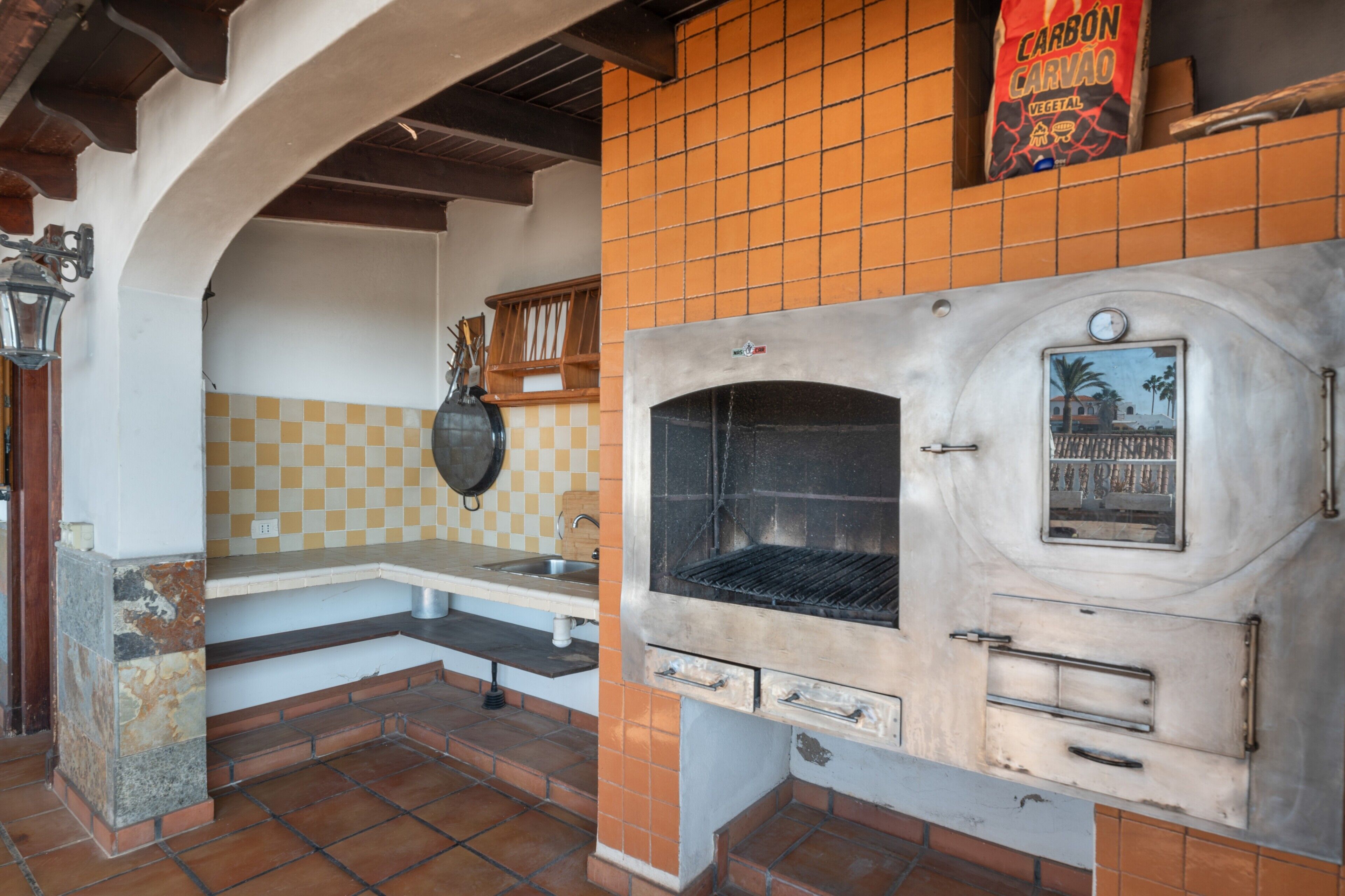 Un área de cocina exterior con horno empotrado, lámpara colgante y salpicadero de azulejos.
