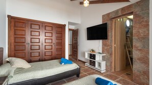 Un dormitorio con cama, armario de madera, televisor y puerta de baño.