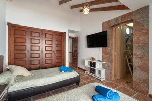 Une chambre à coucher avec un lit, une armoire en bois, une télévision et une porte menant à la salle de bain.