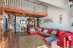 Un'ampia zona giorno con una scala in legno, un grande divano componibile e un lampadario.