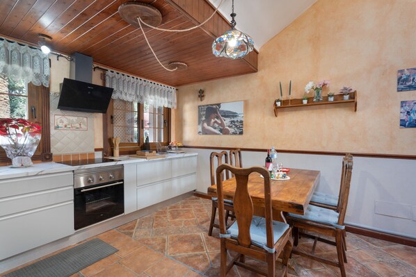 Une cuisine avec un plafond en bois, une table à manger avec des chaises, un téléviseur fixé au mur et une fenêtre avec des rideaux.