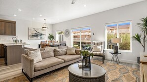 A spacious living room with a sofa, a coffee table, and a dining area with a table and chairs. There is a large window providing a view of the outside. - The Vues 6|Resort Pool, Ping Pong Table, Private Blacony (St. George)