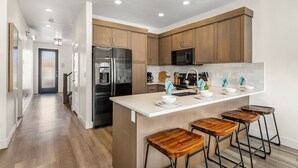 A modern kitchen with wooden cabinets, a stainless steel refrigerator, a microwave, and a large island with bar stools. - The Vues 6|Resort Pool, Ping Pong Table, Private Blacony (St. George)