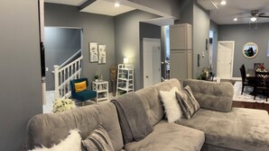 A modern living room with a grey sectional sofa, a small side table, and a staircase leading to another level. - Luxury Fully Furnished Spacious 3 BDR 3 Full BTH Columbus Home with Amenities! (Columbus)