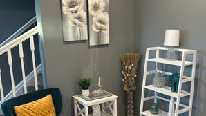 A corner room with a teal armchair, a white side table with decorative items, a white shelving unit, and two floral paintings on the wall. - Luxury Fully Furnished Spacious 3 BDR 3 Full BTH Columbus Home with Amenities! (Columbus)