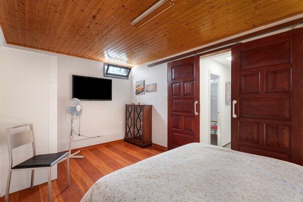 Un dormitorio con cama, televisor montado en la pared, techo de madera y armario.