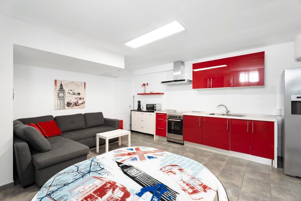 A modern kitchen with red cabinets, a grey sofa, and a table with a Union Jack design.