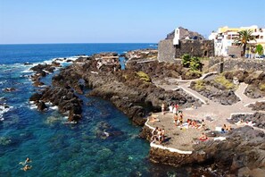 A coastal area with rocky terrain, clear blue water, and a historic building.