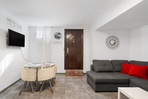 A living room with a TV, a sofa, a dining table with chairs, and a door.
