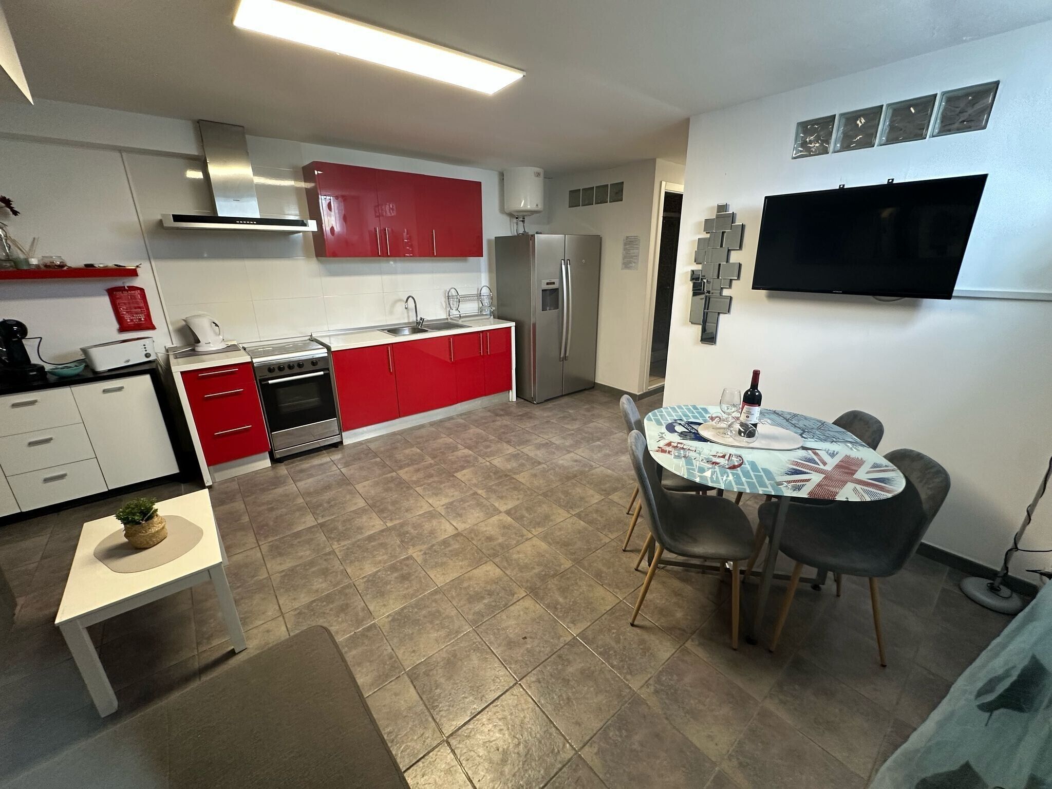 A modern kitchen with red cabinets, a stainless steel stove, and a dining area with a table set for two.