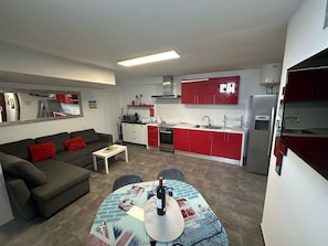 Un espacio habitable compacto con sofá, mesa de comedor, zona de cocina y refrigerador.