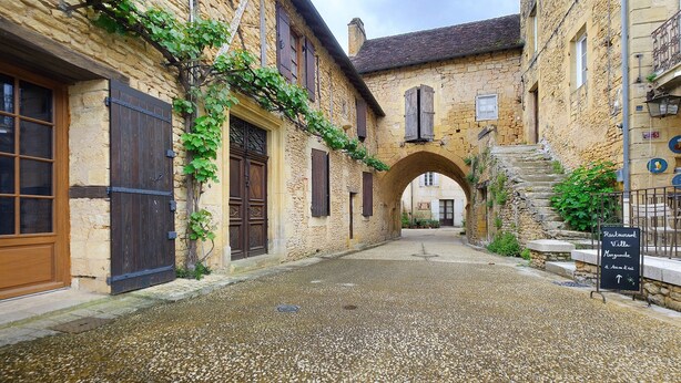 A stone building with a cobblestone courtyard, a sign indicating a restaurant, and an archway. - Gîte De L’Egal – Cadouin, Sleeps 10, Air-Conditioned, Private Pool, Périgord Charm (Le Buisson-de-Cadouin)
