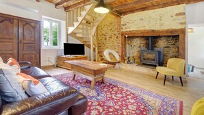 A living room with a wooden ceiling, a staircase, a fireplace, a sofa, a coffee table, and a television. - Gîte De L’Egal – Cadouin, Sleeps 10, Air-Conditioned, Private Pool, Périgord Charm (Le Buisson-de-Cadouin)