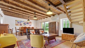 A spacious living room with wooden beams, a sofa, a chair, a coffee table, and a TV. - Gîte De L’Egal – Cadouin, Sleeps 10, Air-Conditioned, Private Pool, Périgord Charm (Le Buisson-de-Cadouin)