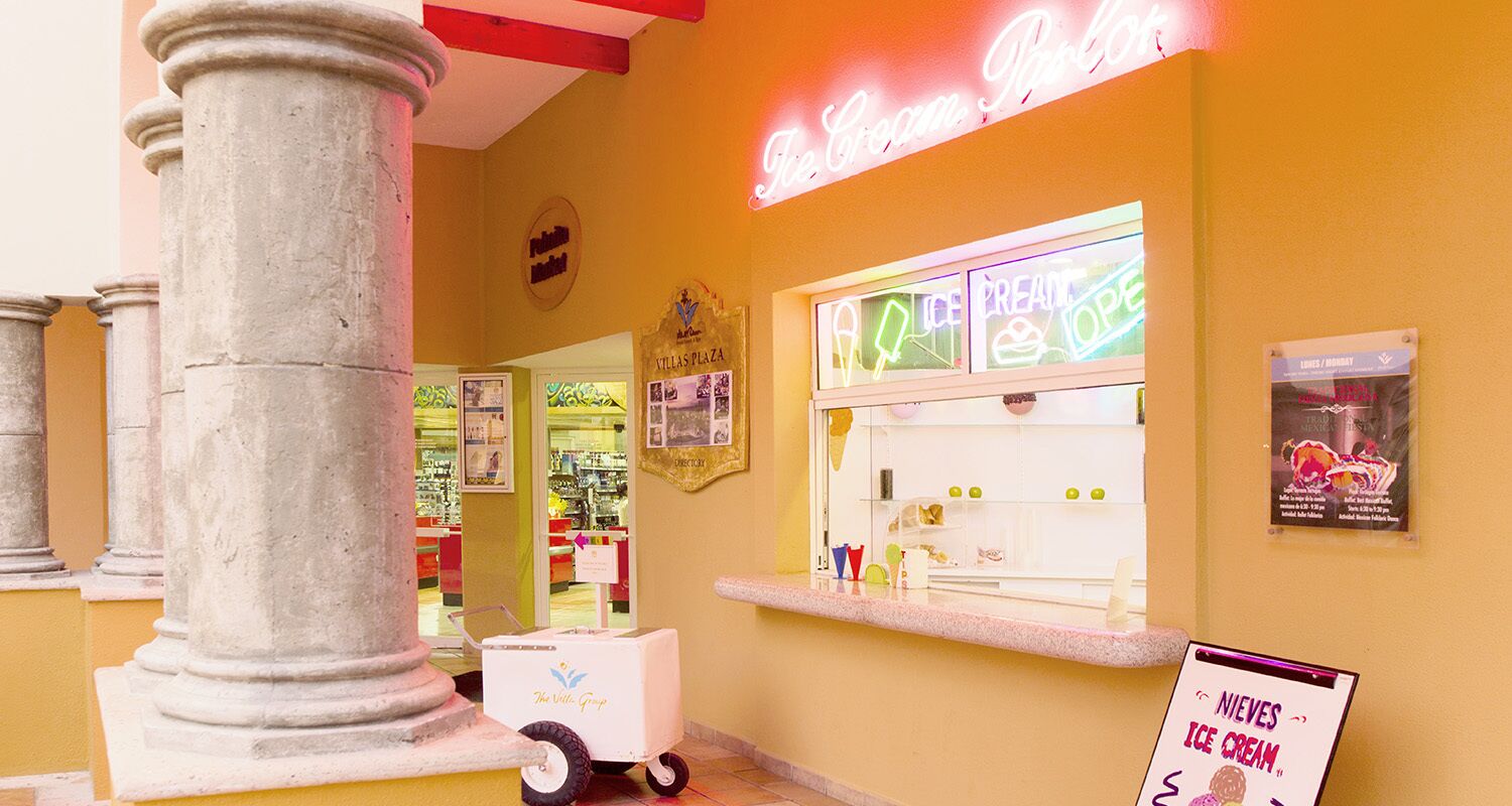 Un magasin de glaces avec une enseigne au néon, un chariot et un panneau affichant le menu.