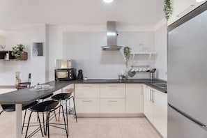 Una cocina moderna con encimera oscura, armarios blancos, una campana extractora de acero inoxidable y un refrigerador.