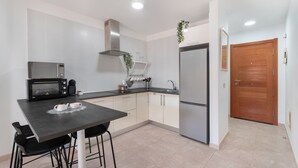 A modern kitchen with a microwave, stove, sink, and refrigerator. There is a dining table with chairs and a hanging plant.