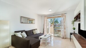 A modern living room with a sofa, a coffee table, a TV, and a balcony with curtains.