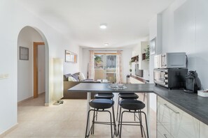 Una cocina moderna con una isla central, taburetes de bar, microondas, tostadora y cafetera.