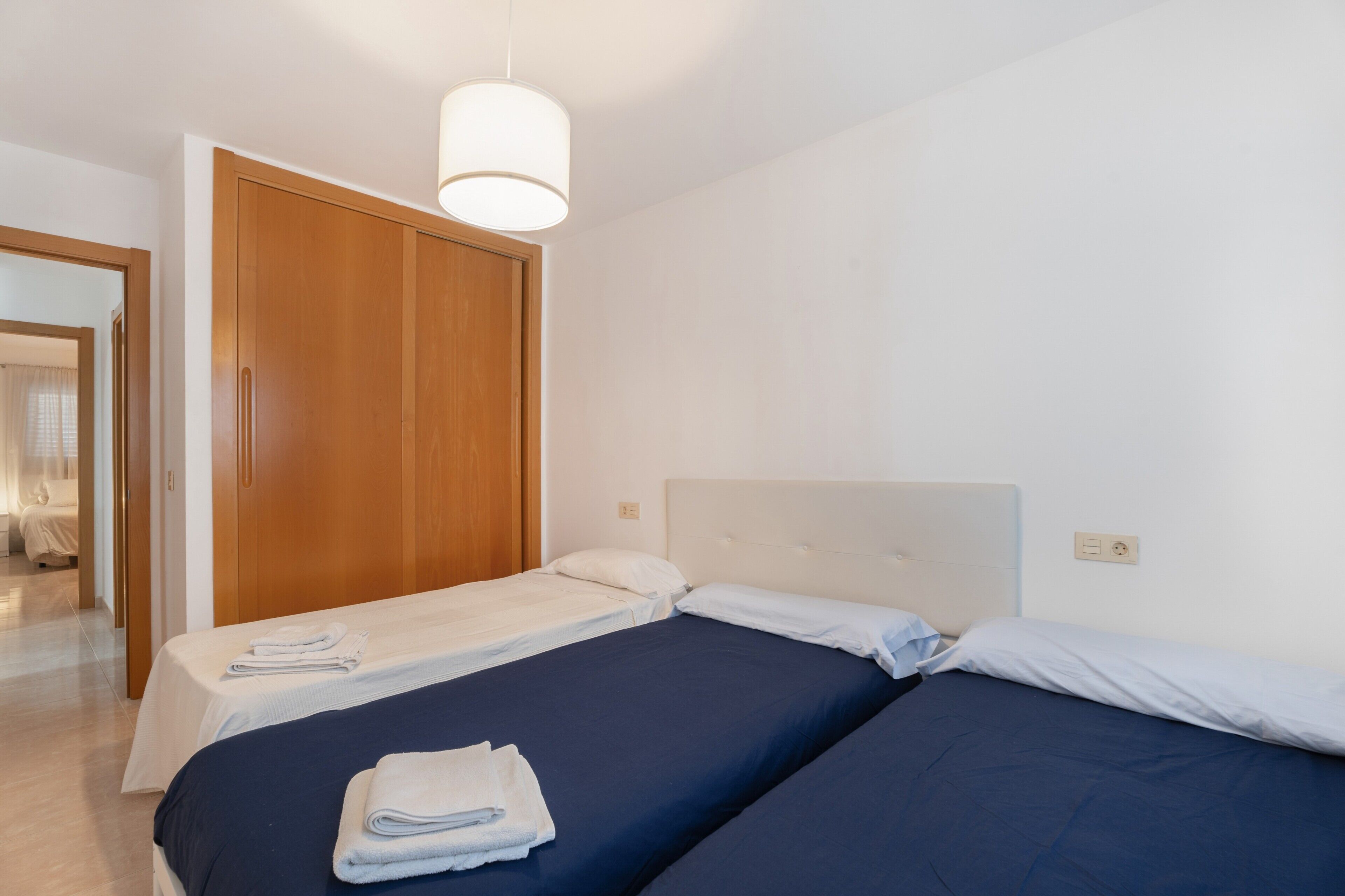 A hotel room with two beds, a wooden wardrobe, and a hanging light fixture.