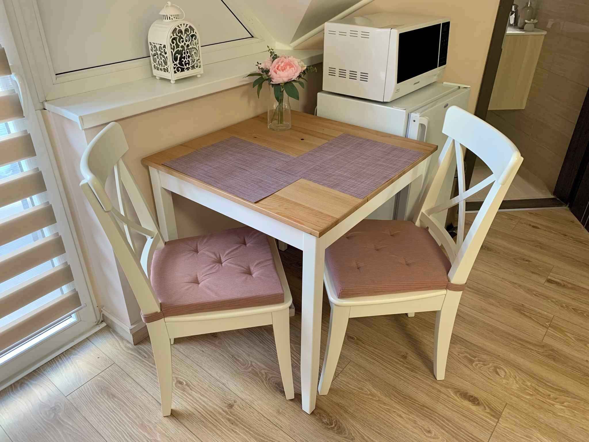 Un pequeño comedor con una mesa de madera, dos sillas, un microondas blanco y un farol decorativo.