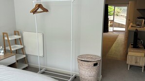 A bedroom with a bed, a white wardrobe, a hanging rack, a small wooden table, and a wicker basket. - Studio Apartment 100 meters from lake and walking track  (Cromwell)