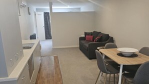 A modern kitchen with a wooden countertop and a sink, a dining area with a table and chairs, and a living space with a sofa and a TV. - Studio Apartment 100 meters from lake and walking track  (Cromwell)