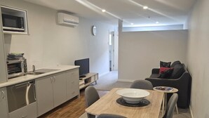 A compact living space with a kitchenette, a dining area with a table and chairs, and a sofa. - Studio Apartment 100 meters from lake and walking track  (Cromwell)