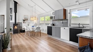 Eine moderne Küche mit einer zentralen Kochinsel, einem Essbereich mit rundem Tisch und einem eingebauten Holzofen.