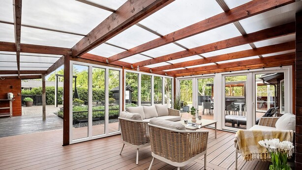 Eine überdachte Terrasse mit Holzboden, Korbmöbeln und Blick auf den Garten.