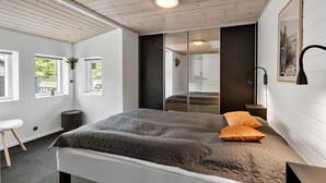 Ein Schlafzimmer mit Bett, Nachttisch, Stuhl, Fenster und einer Tür zu einem anderen Raum.