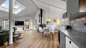 Eine moderne Küche mit einem eingebauten Bosch-Geschirrspüler, einem Essbereich mit weißem Tisch und Stühlen sowie einem großen an der Wand befestigten Fernseher.