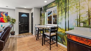 Un coin repas avec une table ronde et des chaises, une porte noire et une fresque murale représentant une scène de forêt.