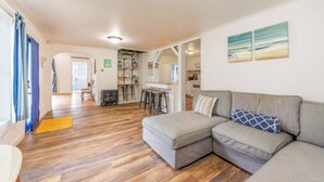 Ein modernes Wohnzimmer mit einem grauen Ecksofa, Holzböden und einer Küchenzeile im Hintergrund.