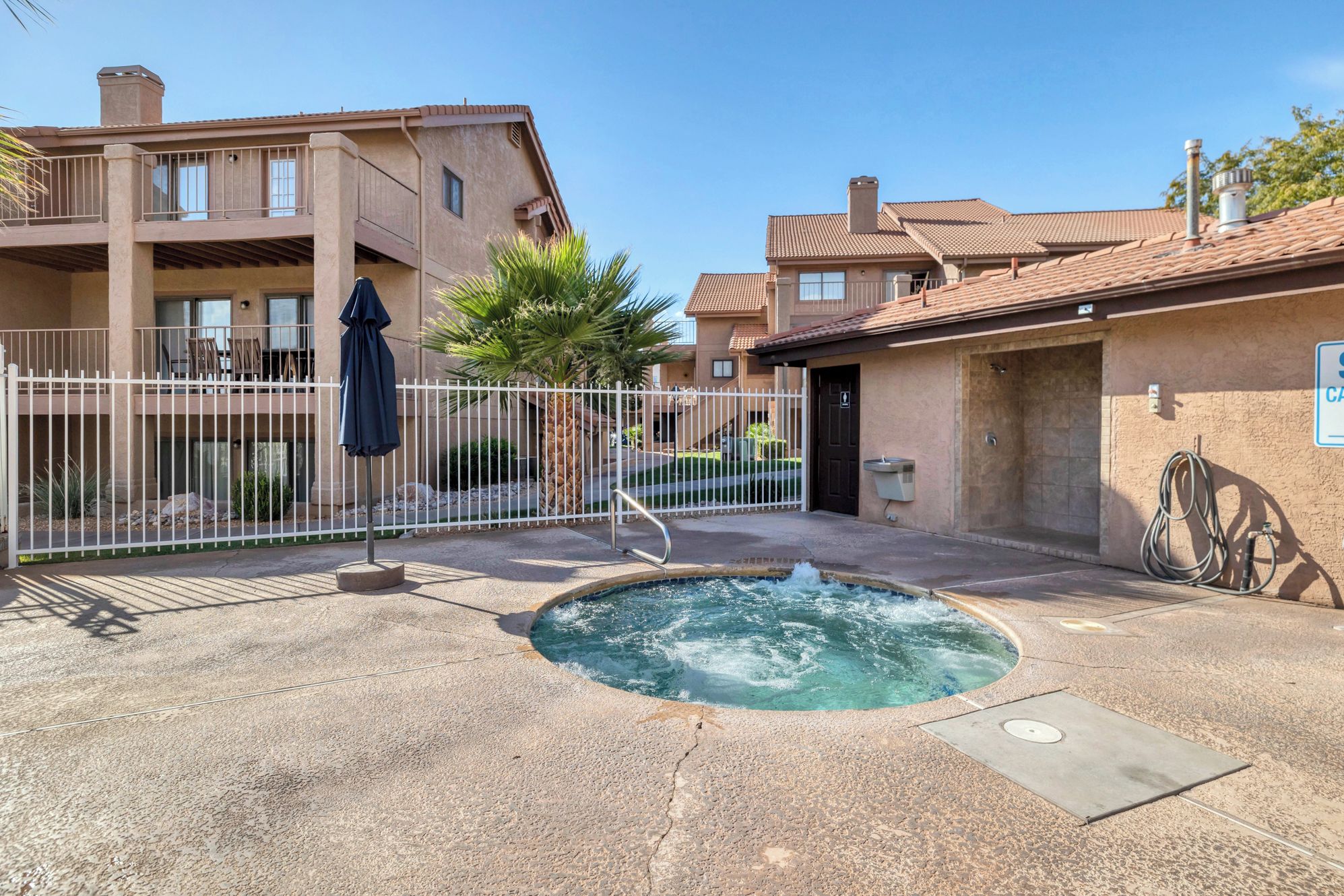 Un espace piscine avec un jacuzzi, une terrasse clôturée et un bâtiment doté d’un toit en tuiles.